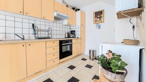 A compact kitchen with wooden cabinets, a black oven, a coffee maker, and a potted plant.