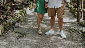 Una pareja parada sobre un camino de grava rodeada de árboles.