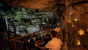 Comedor en una cueva con una mesa de madera rústica, velas y vistas a una formación natural de roca.