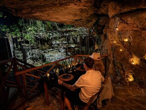 A cave dining area with a rustic wooden table, candles, and a view of a natural cave formation.