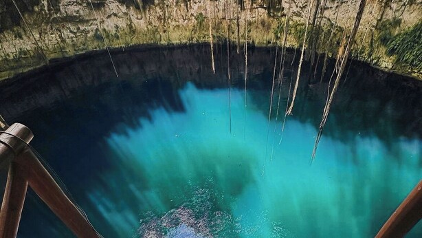 Una persona recostada sobre una plataforma de madera con vistas a una piscina azul cristalina.