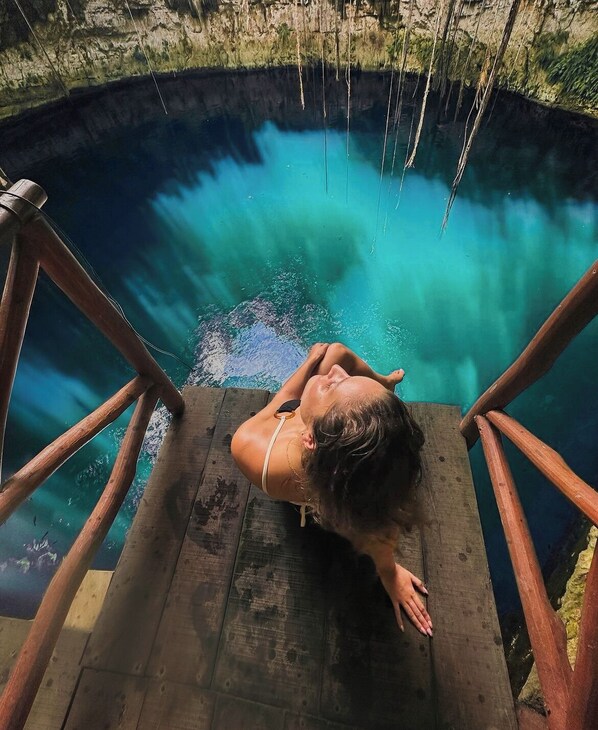 A person lying on a wooden platform overlooking a clear blue pool.