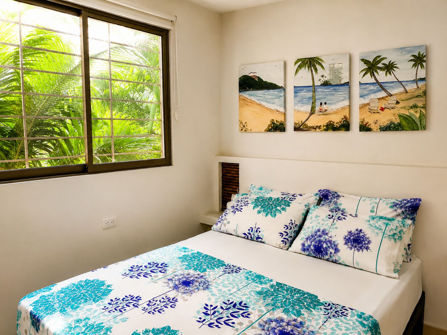 A bedroom with a bed, a window with blinds, and three wall-mounted paintings.