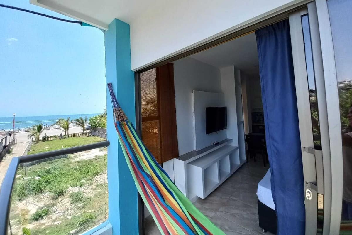 Un balcon avec vue sur la plage, un téléviseur fixé au mur et un rideau bleu.