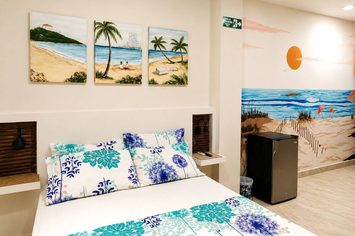 Une chambre d’hôtel comprenant un lit, une table de chevet, une poubelle et une décoration murale représentant une scène de plage.
