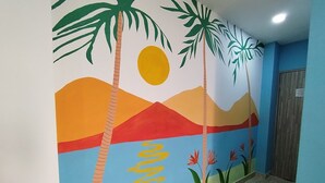 A hallway with a mural of a sunset over mountains, palm trees, and flowers. - Hotel Avadia Del Mar (Cartagena)