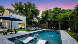 Piscina rectangular con solárium, sillas de descanso y una pérgola.
