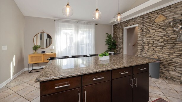 Una cocina con encimera de granito, armarios oscuros, pared decorativa de piedra, consola de madera y un espejo.