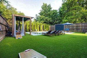 Un patio trasero con una pérgola de madera, piscina, sillones de descanso y una mesa.