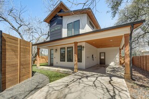 A modern two-story house with a covered patio, a wooden fence, and a well-maintained lawn.