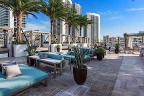 Un salon sur le toit avec des espaces de détente en plein air, des palmiers et une vue sur la ville.