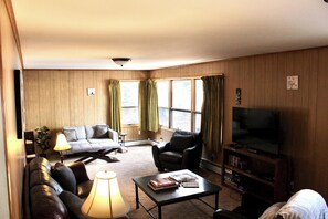 Una sala de estar con sofá, sillón, mesa de centro, lámpara y televisor.