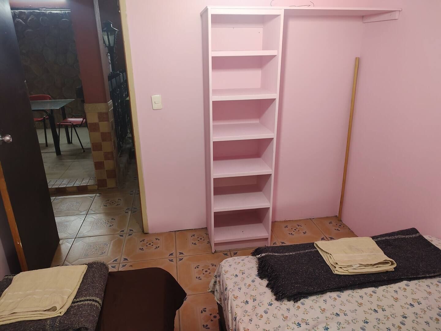 Une petite pièce avec deux lits, une armoire rose et un sol carrelé.