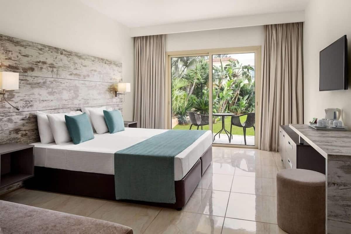 Habitación de hotel con una cama grande, un escritorio, una silla y un balcón con vistas a zonas verdes.