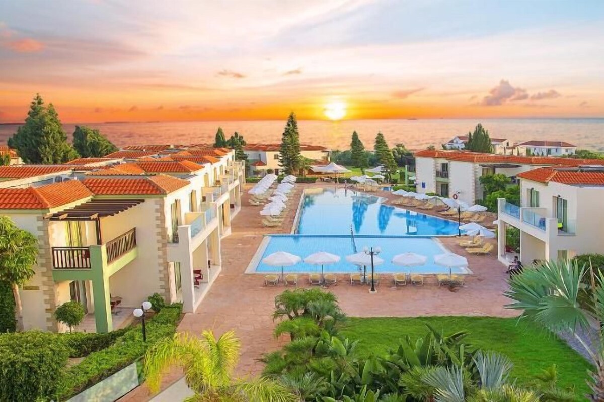 A resort with a swimming pool, multiple buildings, and a sunset view.