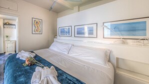 A hotel room with a bed, a ceiling fan, framed artwork on the wall, and a window with a view.