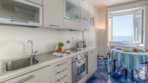 A compact kitchen with a sink, stove, and cabinets, a dining table with chairs, and a view of the sea through a window.