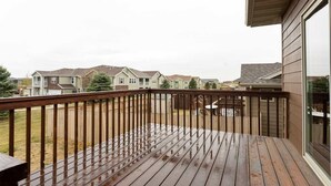 Een houten terras met een balustrade, uitzicht op omliggende huizen, en een heldere lucht.