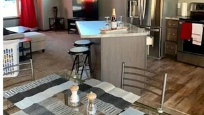 Een moderne keuken met een centraal eiland, roestvrijstalen apparatuur en een eethoek met een tafelkleed met dessin.