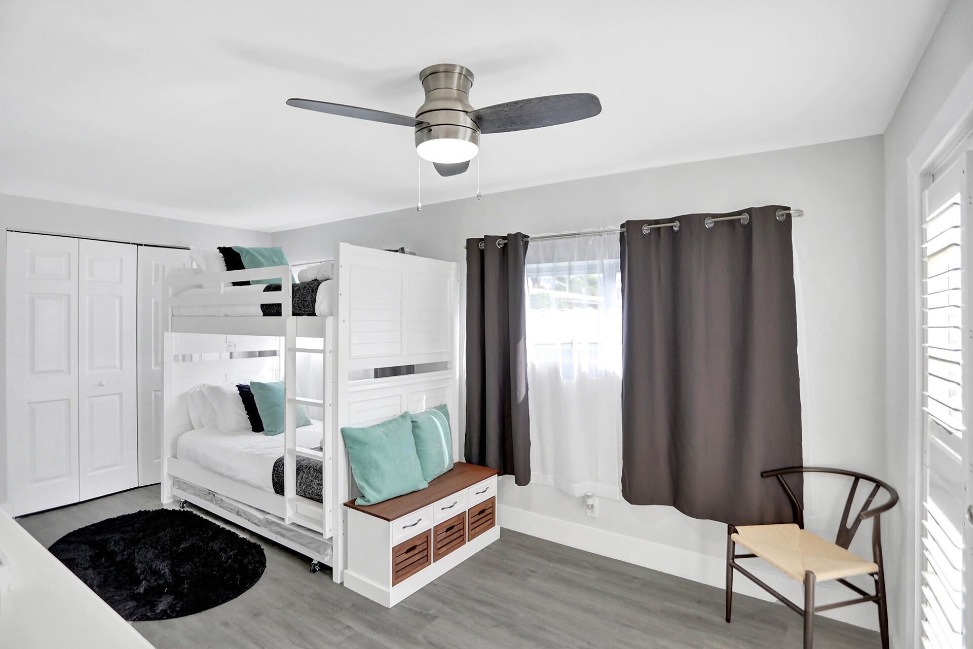 Un lit superposé avec des tiroirs de rangement, un ventilateur de plafond, une chaise et une fenêtre avec des rideaux.