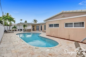 A swimming pool with a curved edge, surrounded by a tiled patio and palm trees. - 6 BR With Heated Pool Close to Beach (Pompano Beach)