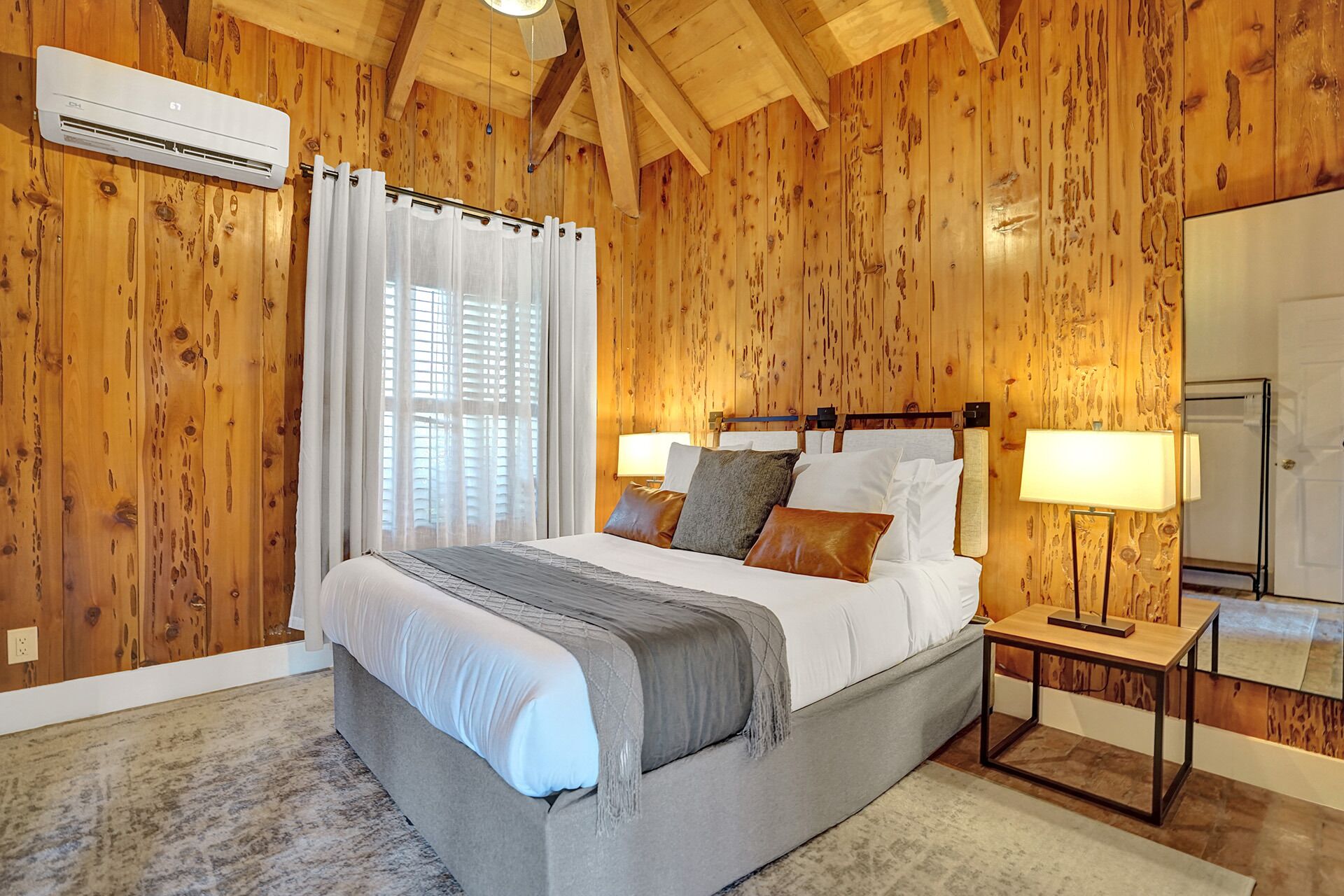 Ein Schlafzimmer mit Holzvertäfelung, einem Bett mit weißer Bettwäsche, einem Nachttisch mit Lampe und einer Klimaanlage.