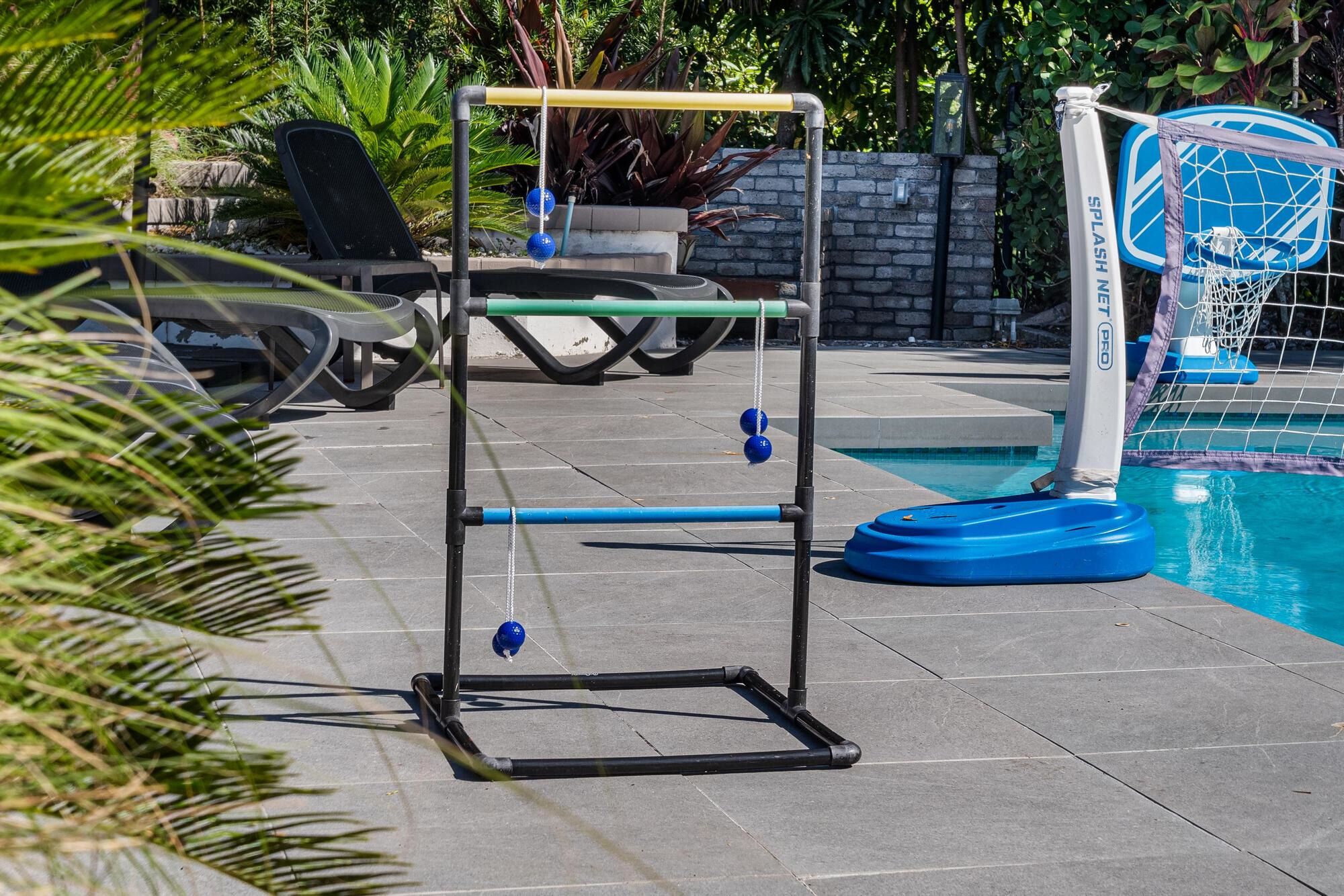 A poolside area with a basketball hoop, lounge chairs, and a pool.