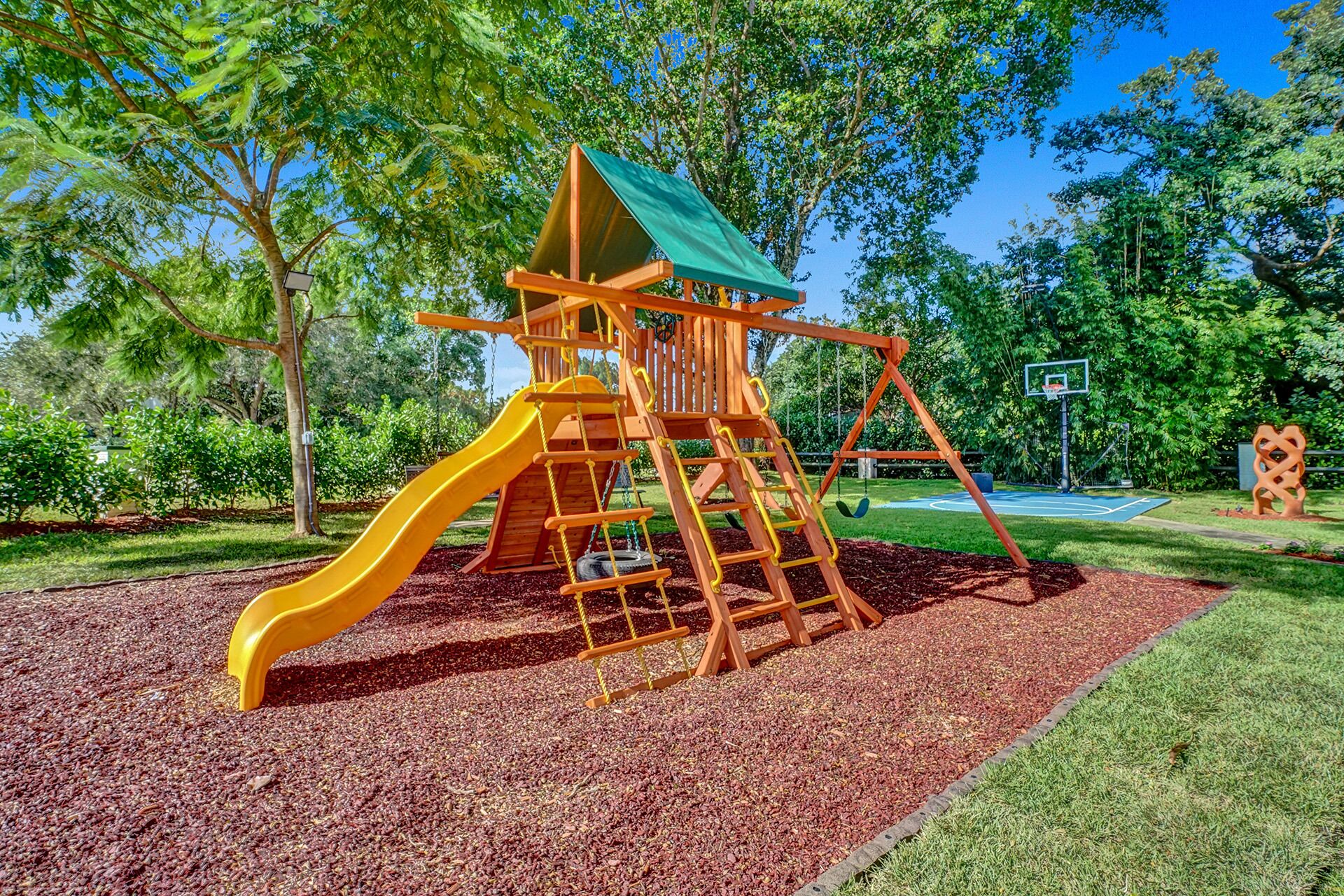 A playground with a slide, climbing structures, and a basketball court.