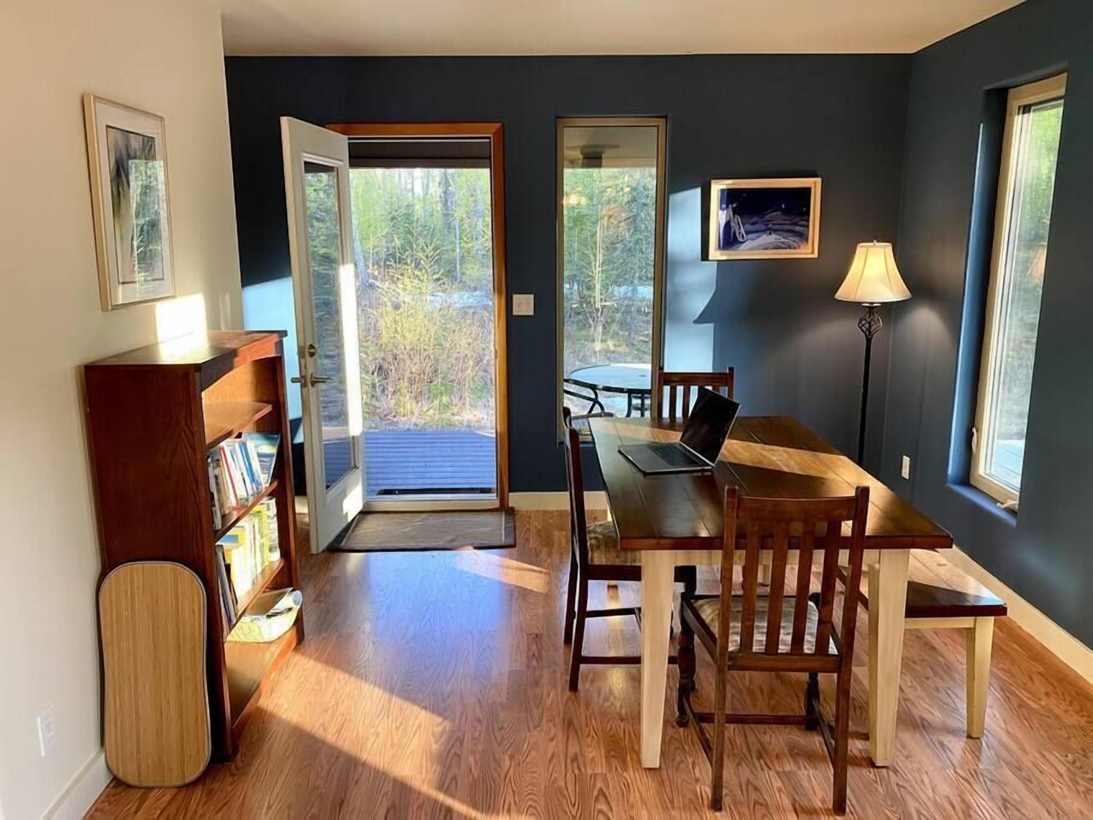 A dining area with a wooden table and chairs, a laptop on the table, and a bookshelf.