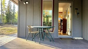 Eine Holzterrasse mit Tisch und Stühlen, eine Tür zu einem Innenraum und Blick auf Bäume.