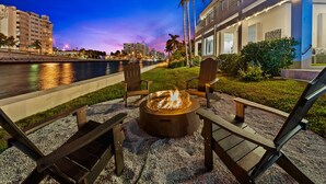 An outdoor seating area with a fire pit, two Adirondack chairs, and a view of a river and cityscape at dusk. - Intercostal beauty with heated pool + Spa! (Hollywood)