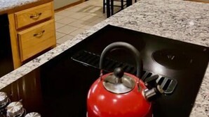 Una cocina con encimera de granito, armarios de madera, un hervidor rojo y un comedor con mesa y sillas.
