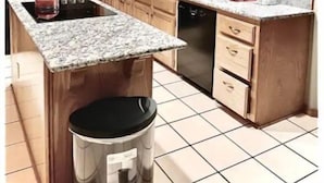 Una cocina con armarios de madera, encimera de granito, refrigerador negro, un lavamanos y lavavajillas.