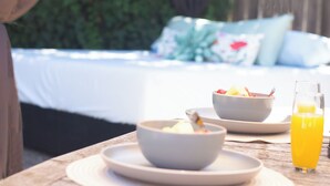 A breakfast setup with bowls of cereal and fruit, a glass of orange juice, and a bed with pillows in the background. - Large home - Sleeps many 4B/2B (Walnut Creek)