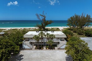Ein Strandhotel mit einer zweistöckigen Struktur, einem zentralen Innenhof mit Palmen und Blick auf Strand und Meer.