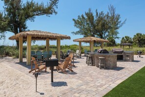 Eine Terrasss mit Strohdächern, Holzstühlen und einem Grillplatz.