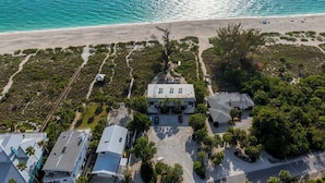 Vue aérienne d’une propriété située sur la côte, avec une grande maison, une plage et un espace de stationnement.