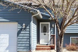 A house with a garage door, a front door, and a tree in front.