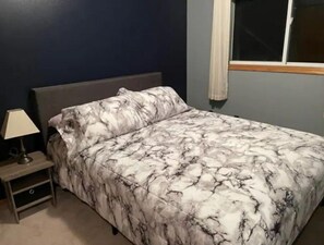 A bedroom with a bed, a nightstand, and a window.