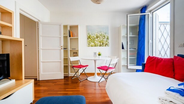 Habitació d'hotel amb llit, televisió, escriptori, cadira, taula petita i finestra amb cortines.