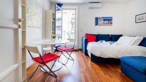 Habitació senzilla amb llit, taula de dinar amb cadires, petita cuina i un balcó amb vistes.