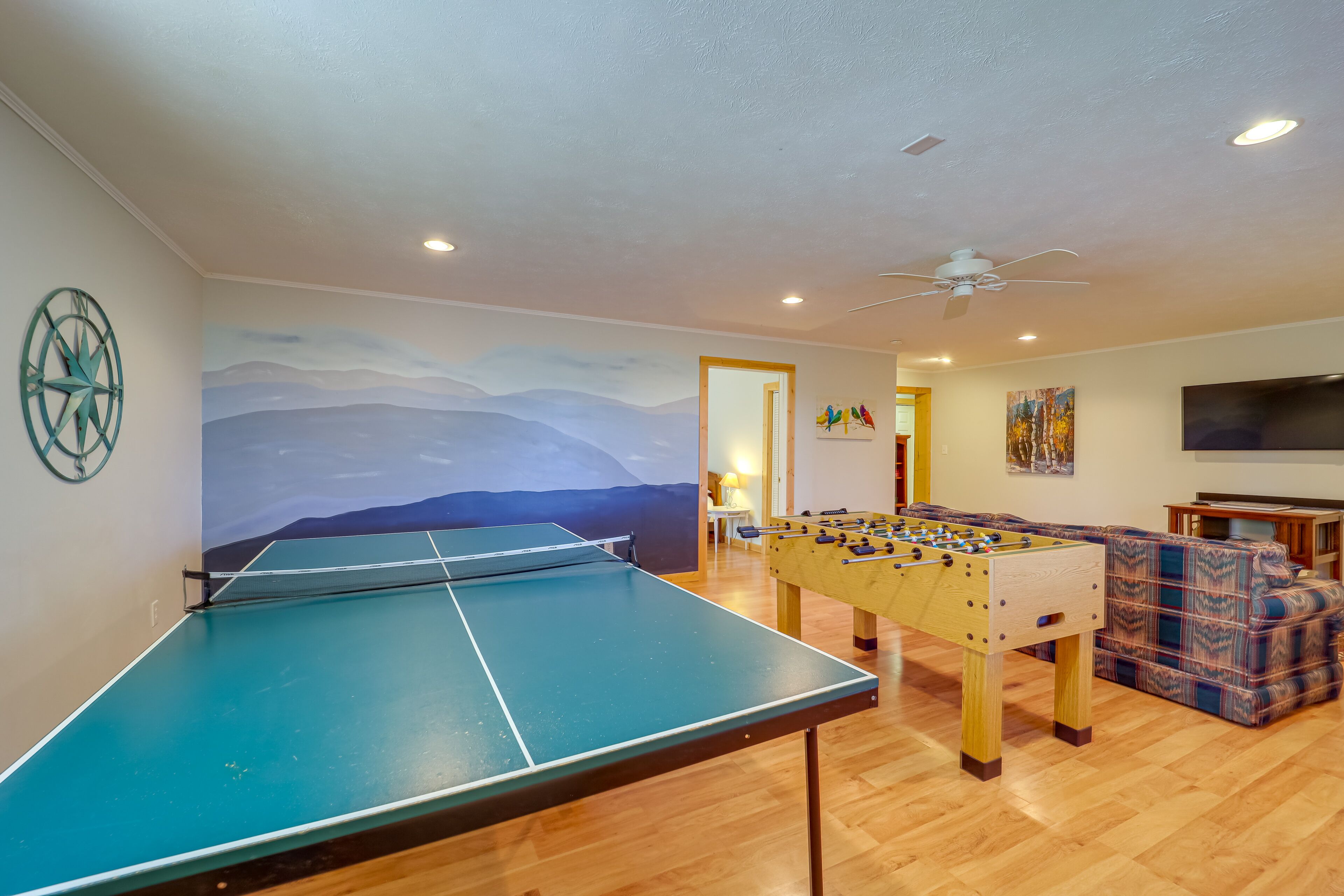 A room with a ping pong table, foosball table, and a sofa.