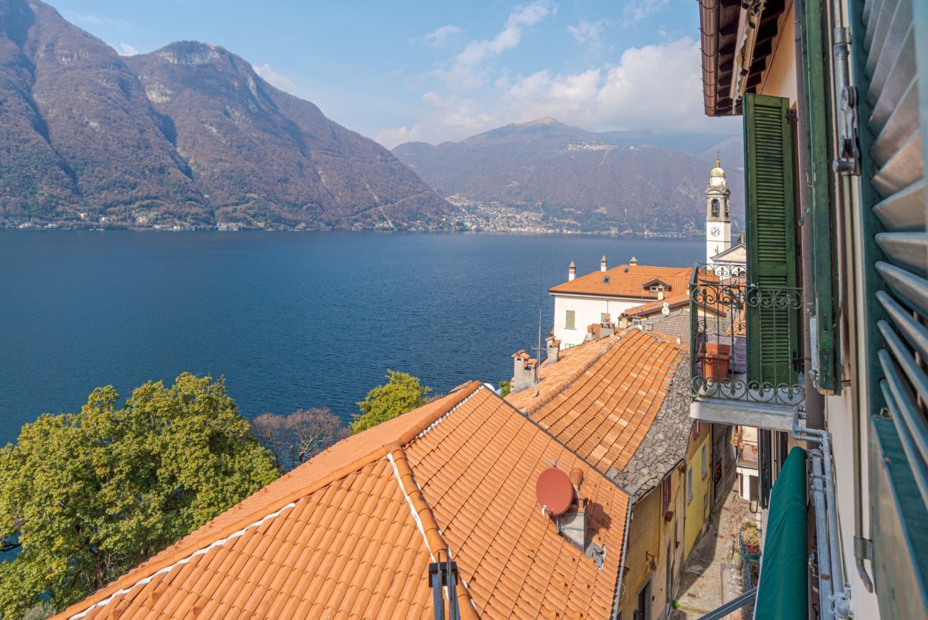 A view of a lake with mountains in the background, a building with a red-tiled roof, and a bell tower.