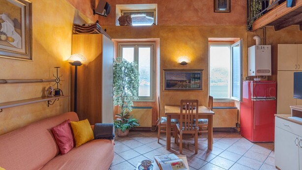 Un salon chaleureux avec un canapé, une table à manger, des chaises, un réfrigérateur rouge, une plante en pot et une fenêtre donnant sur un beau paysage.
