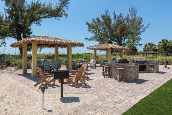 An outdoor patio with thatched umbrellas, wooden chairs, and a barbecue area.