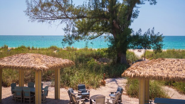 Ein Sitzbereich am Strand mit Reetdach-Sonnenschirmen, Stühlen und einem Tisch.