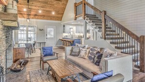 A spacious living area with a wooden staircase, a kitchen in the background, and a dining area with a view. - Lake Cove Oasis - Waterfront on Lake Blue Ridge | Private Yard and Dock | Pet Friendly (Morganton)