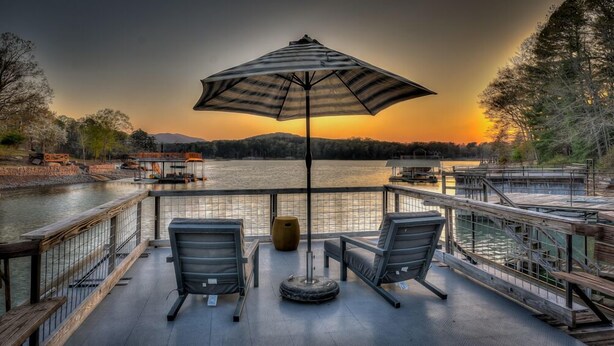 A deck with two chairs and a table, overlooking a lake with a sunset. - Lake Cove Oasis - Waterfront on Lake Blue Ridge | Private Yard and Dock | Pet Friendly (Morganton)