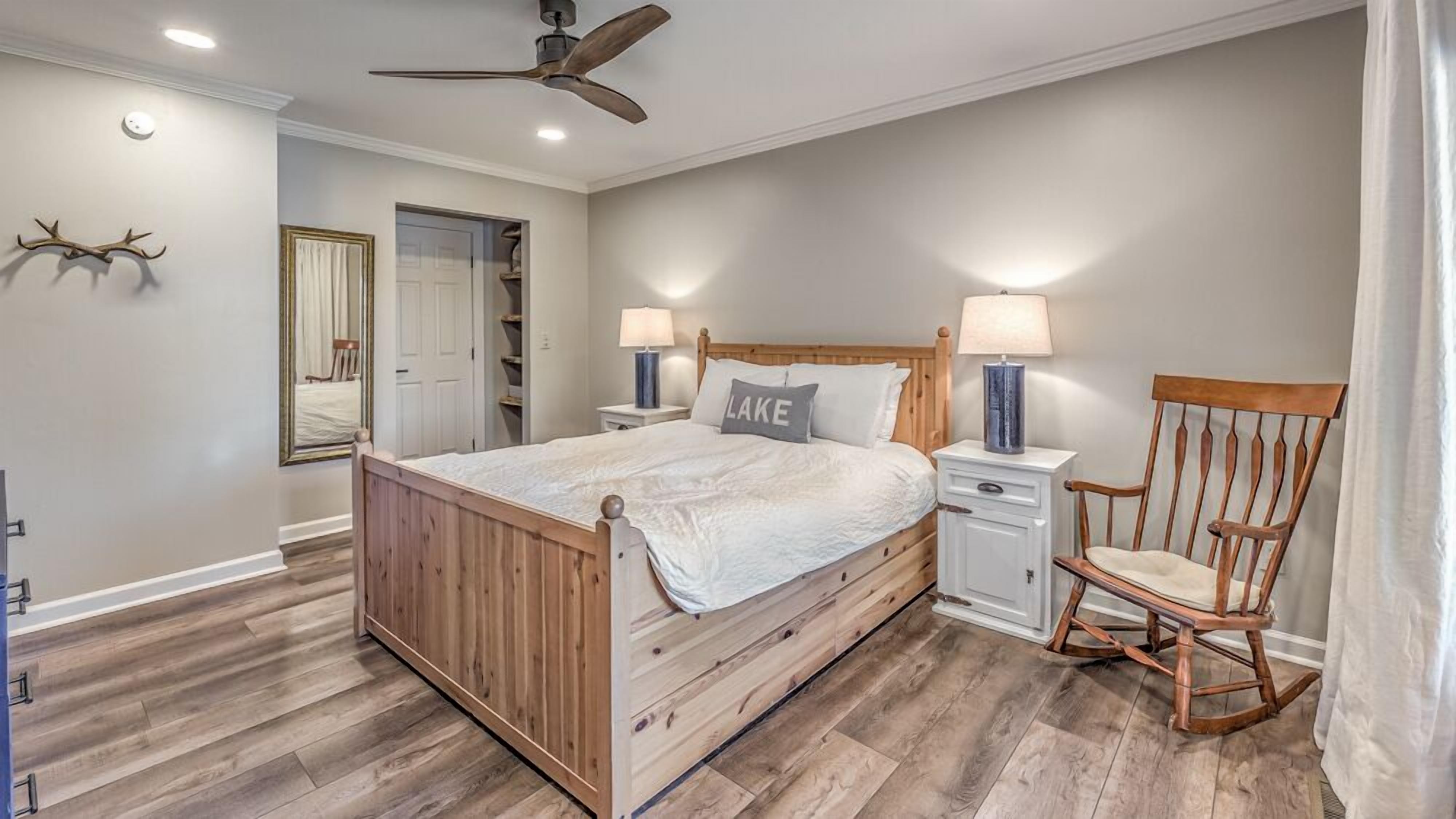 A bedroom with a wooden bed, nightstands, a chair, a ceiling fan, and a mirror.