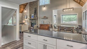 A modern kitchen with a stone fireplace, wooden ceiling, and large windows. - Lake Cove Oasis - Waterfront on Lake Blue Ridge | Private Yard and Dock | Pet Friendly (Morganton)